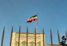 Iranian flag waving above a government building against a blue sky