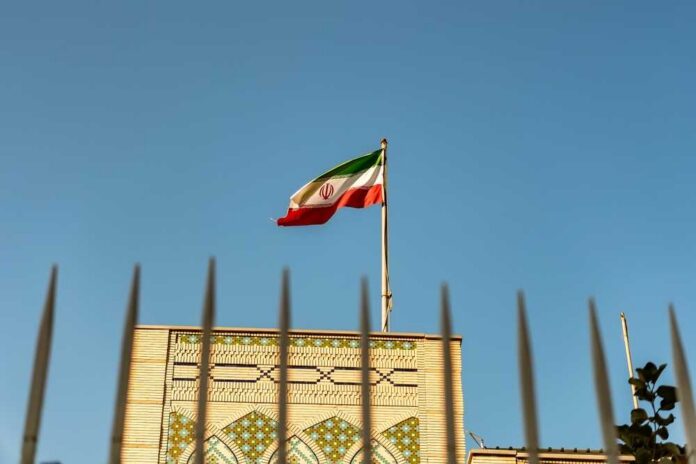 Iranian flag waving above a government building against a blue sky