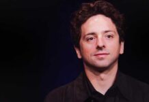 A man with curly hair smiling against a dark background