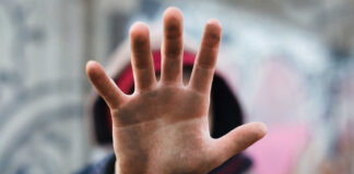 A close-up of a hand held up in front of a person against a graffiti background
