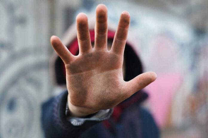 A close-up of a hand held up in front of a person against a graffiti background