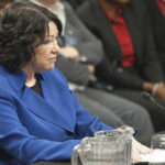 A woman in a blue blazer sitting at a table during a formal hearing