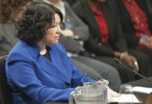A woman in a blue blazer sitting at a table during a formal hearing