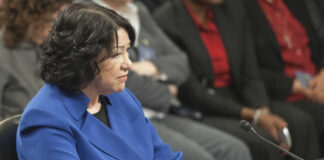 A woman in a blue blazer sitting at a table during a formal hearing
