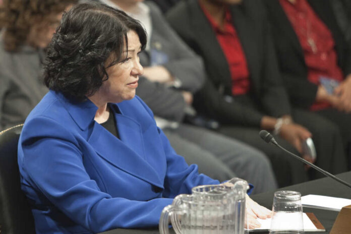 A woman in a blue blazer sitting at a table during a formal hearing