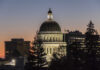 Illuminated dome of a government building against a sunset sky