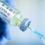 Ebola Vaccine Trial: COVID Controversy Repeats? Gloved hand holding COVID19 vaccine vial and syringe