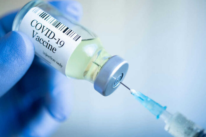 Gloved hand holding COVID19 vaccine vial and syringe