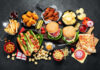Assorted fast food including burgers, hot dogs, wings, fries, and pizza on a dark table