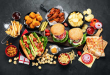 Assorted fast food including burgers, hot dogs, wings, fries, and pizza on a dark table