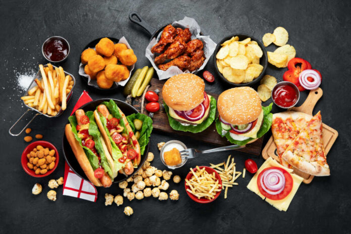 fast-food-and-unhealthy-eating-concept2182172665jpg Assorted fast food including burgers, hot dogs, wings, fries, and pizza on a dark table