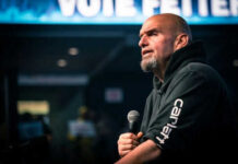 Democrats’ Wild Conspiracy: Fetterman Says “ENOUGH” Man speaking into microphone on stage.