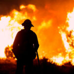 Firefighter silhouetted against massive wildfire flames