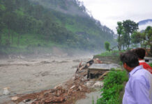 Men observe flood-damaged riverside buildings and debris