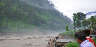 Men observe flood-damaged riverside buildings and debris