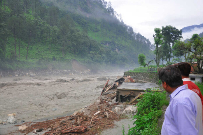 Men observe flood-damaged riverside buildings and debris