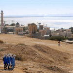 A group of women in blue walking in a desert landscape with historical buildings in the background