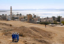 A group of women in blue walking in a desert landscape with historical buildings in the background