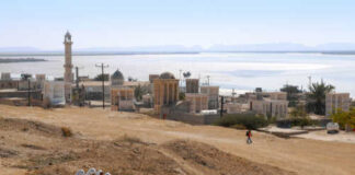 A group of women in blue walking in a desert landscape with historical buildings in the background