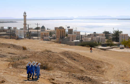 A group of women in blue walking in a desert landscape with historical buildings in the background
