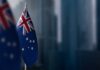Politicized Apologies Stir National Backlash Australian flag displayed on a flagpole with a blurred city background