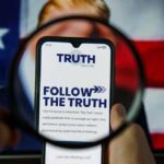 A smartphone displaying the TRUTH Social app, viewed through a magnifying glass