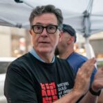 Person clapping at a protest wearing a Writers Guild of America t-shirt
