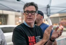 Colbert’s Fate Tied to Trump’s Power Play? Person clapping at a protest wearing a Writers Guild of America t-shirt