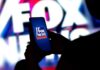 A person holding a smartphone displaying the Fox News logo against a colorful background