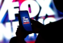 A person holding a smartphone displaying the Fox News logo against a colorful background