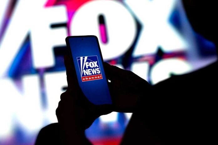 A person holding a smartphone displaying the Fox News logo against a colorful background