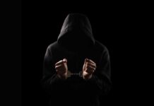 Green Bay’s Jacobs: Arrest Sparks Media Frenzy A hooded figure with hands in handcuffs against a dark background