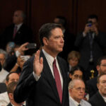 A man raising his right hand in a congressional hearing setting