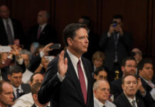 A man raising his right hand in a congressional hearing setting