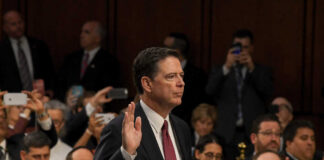 A man raising his right hand in a congressional hearing setting