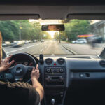 Seven-Year-Old Ejected — Hunt For Phantom Driver Driver holding steering wheel on a city street at sunset