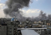 Cityscape with smoke rising, buildings, and a mosque.