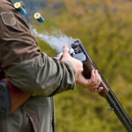 Person reloading shotgun outdoors with cartridges ejecting