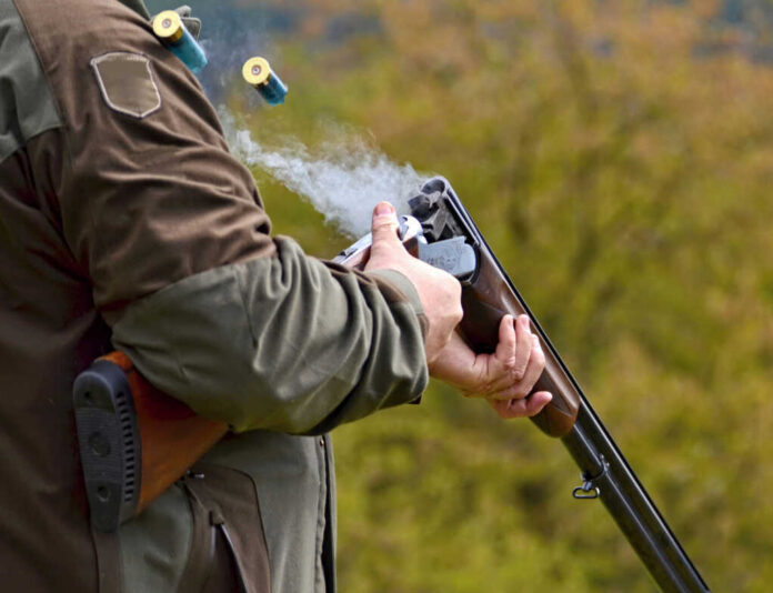 Person reloading shotgun outdoors with cartridges ejecting