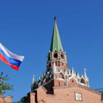 Russian flag and Kremlin tower against a clear blue sky
