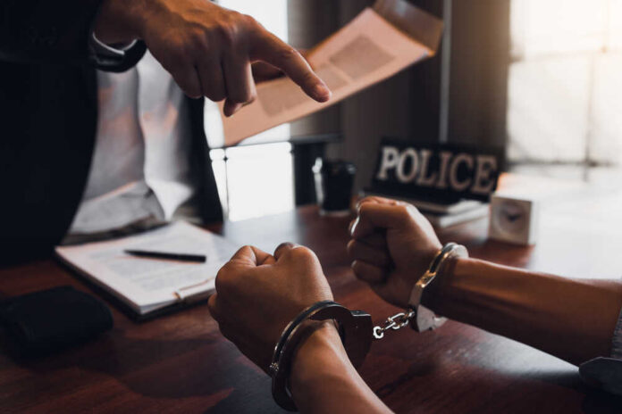 The,Police,Officer,Pointed,The,Handcuffs,And,Held,The,Documents A person in handcuffs being confronted by a police officer