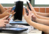 UK Drops Hammer: Under-16s Locked Out Students' hands holding smartphones in a classroom