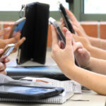 Students' hands holding smartphones in a classroom
