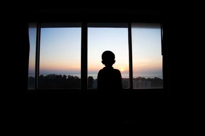 Boy,Silhouette,Standing,And,Watching,The,Morning,Sun,Rise,In Silhouette of a child looking out a window at a sunset