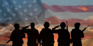 Silhouetted soldiers saluting against an American flag backdrop at sunset