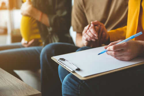 Pregnant woman couple and counselor with clipboard writing