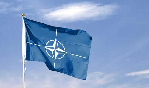 2410731421 Blue NATO flag with white emblem under cloudy sky.