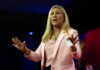 Woman speaking on stage wearing pink blazer