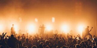 Rock band performing on stage with bright backlights and cheering crowd