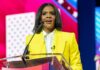 MAGA Darling Makes Her Biggest Political Break A woman in a yellow blazer speaking at a podium with a microphone